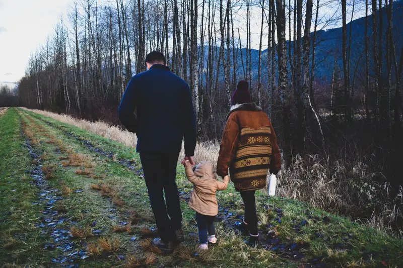 Family walking hand in hand along a forest path on a cool autumn day.