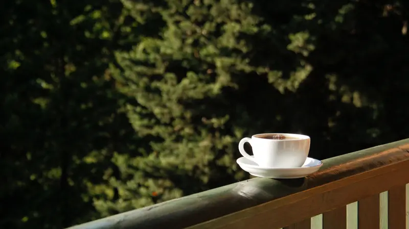 A cup of coffee resting on a porch rail