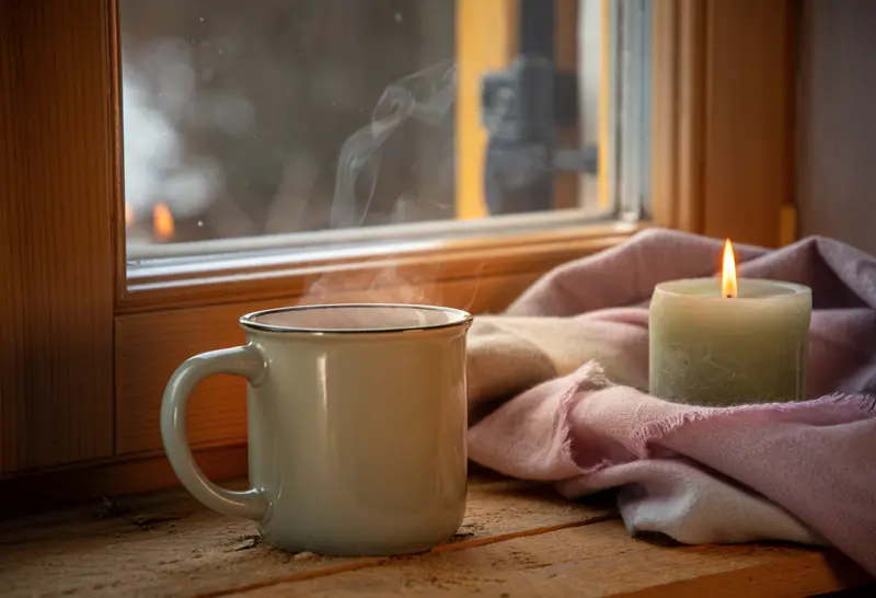 A warm cup of coffee and a candle create a cozy ambiance by the window.