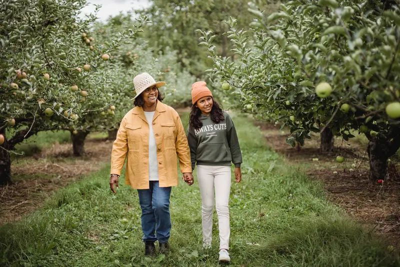 A mother and daughter walking hand in hand between rows of trees
