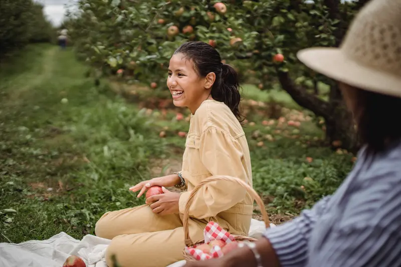 A woman in a straw hat at an orchard picnic, apple in hand