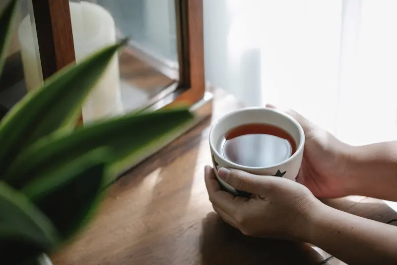 From above of crop anonymous person warming hands with hot cup of aromatic tea
