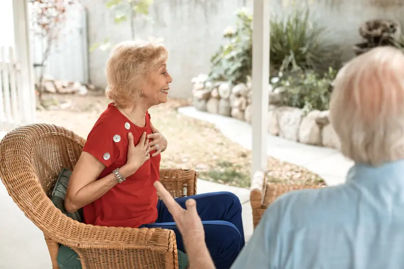 Senior woman in red shirt smiling and conversing in a garden setting.