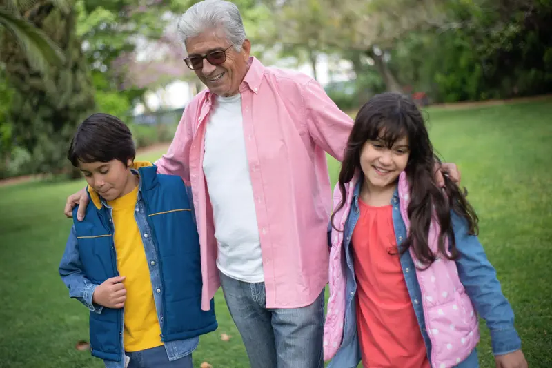 Happy grandfather bonding with grandchildren in a lush park, enjoying a joyful day outdoors.