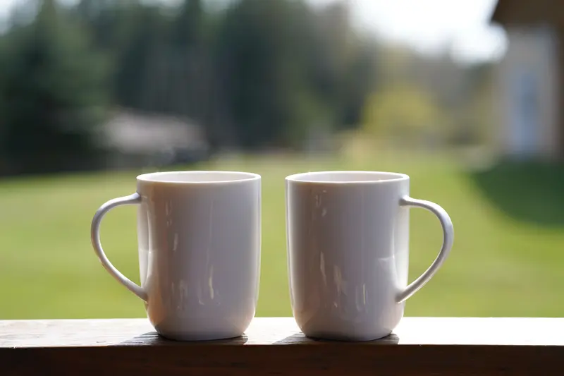 Two white mugs on a porch rail